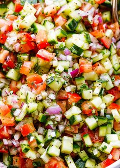 cucumber, tomato and onion salad in a white bowl with a serving spoon