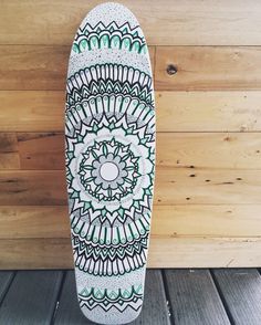 a white skateboard with green and white designs on it's back end against a wooden wall