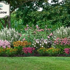 a sign that is in the middle of some flowers and grass with trees behind it