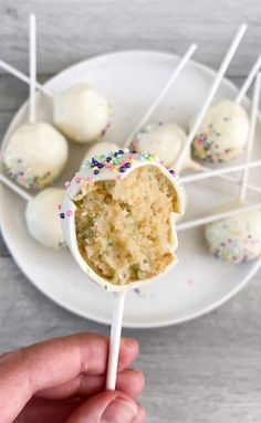 cake pops with sprinkles are on a white plate and there is a hand holding one