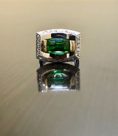 an emerald and diamond ring sitting on top of a table