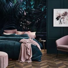 a bedroom with dark green walls and wooden flooring, an upholstered bed is surrounded by pink velvet chairs