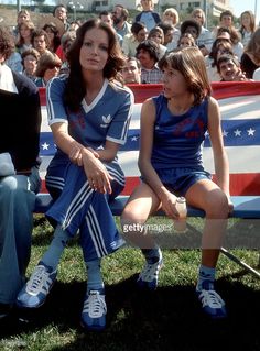 two women sitting on a bench in front of an american flag and people watching them