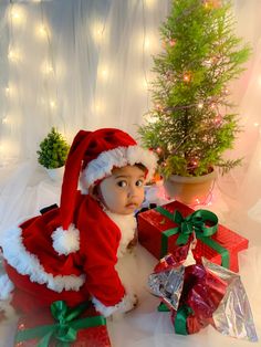 a baby dressed as santa clause sitting next to presents