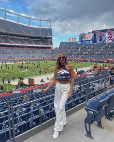 a woman standing in the stands at a football game wearing white pants and a crop top