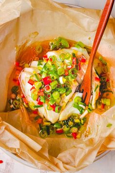 a bowl filled with soup and vegetables on top of a wooden spoon in some brown paper