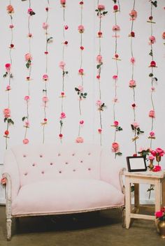 a pink couch sitting in front of a white wall with flowers hanging from it's sides