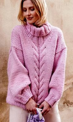 a woman in a pink sweater and white pants is holding a purple bag while standing next to a wall