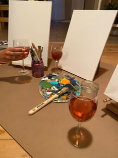 two glasses of wine are sitting on a table with art supplies in front of them