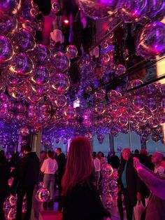 people are gathered in an art gallery with large bubbles hanging from the ceiling and purple lighting