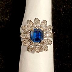 a woman's hand with a ring on it that has a blue stone surrounded by white diamonds