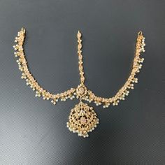 A dazzling fusion of tradition and modern allure! Elevate your style with this enchanting ensemble that seamlessly blends the richness of clear zircons with the classic charm of faux pearls. Pair our Mewish Mathapatti with Mewish Set for a alluring look. Gold-plated on high-quality brass as the base metal. Made by order. Kindly allow 5-7 weeks for the delivery of this item. For custom or urgent requests, please contact support@alacouture.com. *Please Note: We use faux stones and beads in all of Hanging Beads, Heritage Jewellery, Jewellery Gold, Waist Chain, Faux Stone, Head Accessories, Base Metal, Ring Gift, Anklets