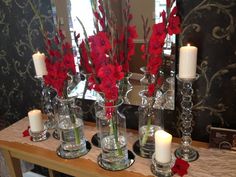 three vases with flowers and candles are on a table in front of a mirror