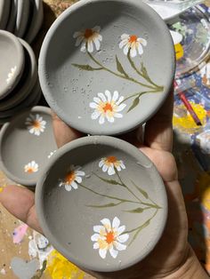 two bowls with daisies painted on them are being held by someone's hand