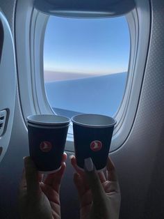 two people holding up cups in front of an airplane window