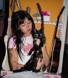 a woman sitting in a chair holding a black and brown cat next to guitar strings