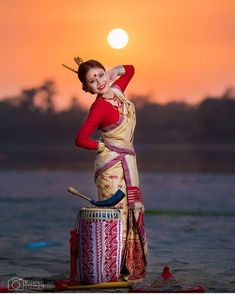 a woman is standing on top of a drum at the beach with her arms in the air