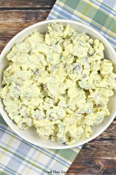 a white bowl filled with potato salad on top of a wooden table next to a blue and green checkered napkin