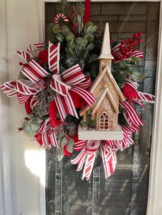 a christmas wreath with a church on top and red ribbon around the front door for decoration