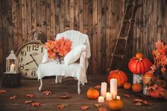 a white chair sitting on top of a wooden floor next to pumpkins and candles