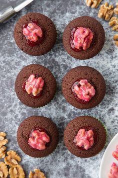 chocolate cupcakes with pink frosting and walnuts next to them on a table