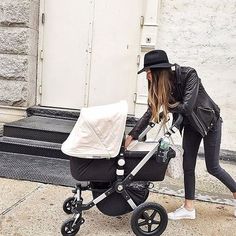 a woman pushing a stroller with a baby in it on the sidewalk next to a building