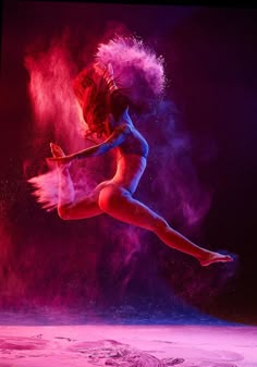 a woman is dancing in the air with colored powder on her body