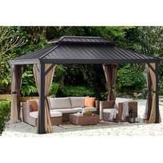 an outdoor gazebo with curtains on the sides and furniture around it in front of some bushes