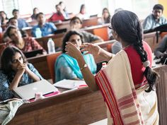 a woman standing in front of a class room full of people sitting at desks