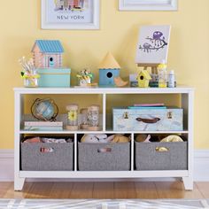 a white shelf with baskets on top of it next to a yellow wall and pictures