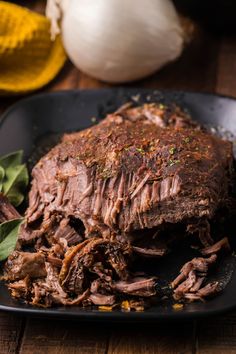 a black plate topped with meat and greens on top of a wooden table next to garlic