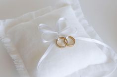 two gold wedding rings tied to a white ring pillow on top of a white blanket