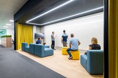 three people are sitting on couches in an office with yellow drapes and blue chairs