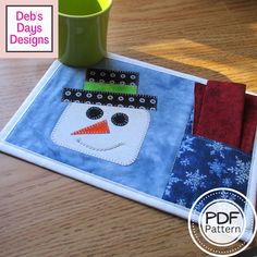 a table mat with a snowman on it next to a coffee cup and mug