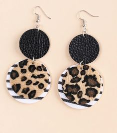 the leopard print and black circle earrings are hanging from leather earwires on a beige background