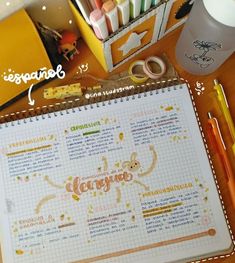 an open notebook sitting on top of a wooden table next to markers and pencils