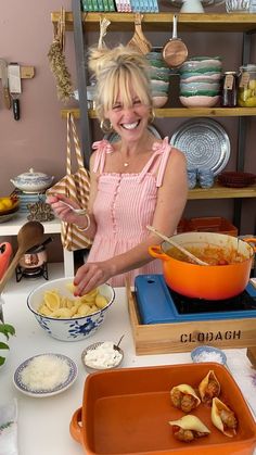 a woman in pink shirt preparing food on top of a white kitchen counter with bowls and pans