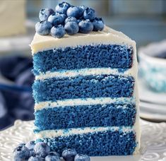 a slice of blue cake with white frosting on a plate next to some blueberries