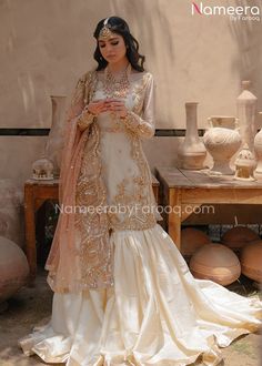 a woman in a white and gold outfit looking at her cell phone while standing next to vases