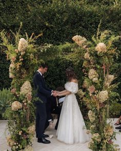 a bride and groom standing in front of a floral arch