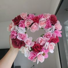 a person holding up a heart shaped wreath with pink and red flowers