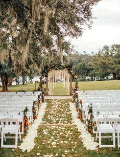 an outdoor ceremony setup with white chairs and greenery on the aisle, surrounded by trees