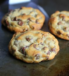 three chocolate chip cookies sitting on top of a cookie sheet