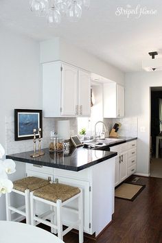 a kitchen with white cabinets and black counter tops, an island in between two stools