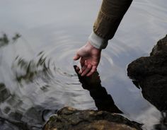 a person reaching for something in the water with their hand on top of some rocks