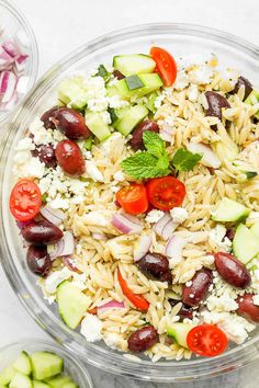 a glass bowl filled with rice, cucumbers and tomatoes next to other vegetables