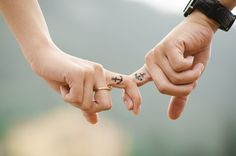 two people holding hands with tattoos on their fingers