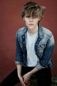 a young man sitting on top of a bench wearing a jean jacket and black pants