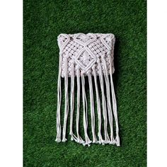 a white crocheted bag on green grass with fringes and beads hanging from it