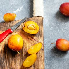 some fruit on a wooden cutting board with a knife next to it and two peaches